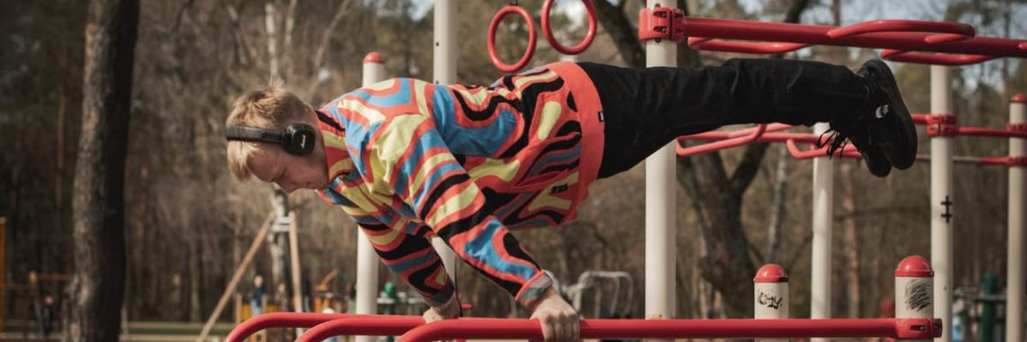 Young adult man exercises on outdoor gym bars in a colorful outfit in Vilnius, Lithuania.